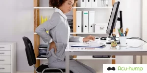 A black woman is experiencing piriformis syndrome pain with one hand on her lower back from sitting at a desk